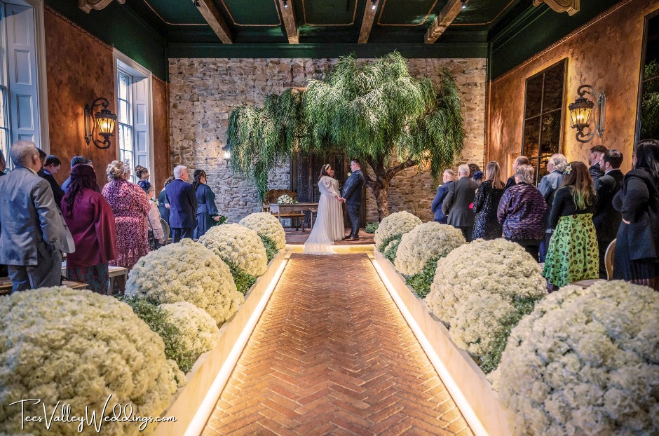 A newlywed couple stands hand in hand at the end of a grand, elegant aisle inside The Croft Hotel in Darlington. With smiles full of love and joy, they embrace the magical atmosphere of one of The Apartment Group’s stunning wedding venues in the North East. The scene radiates romance, promising a lifetime of happiness ahead.