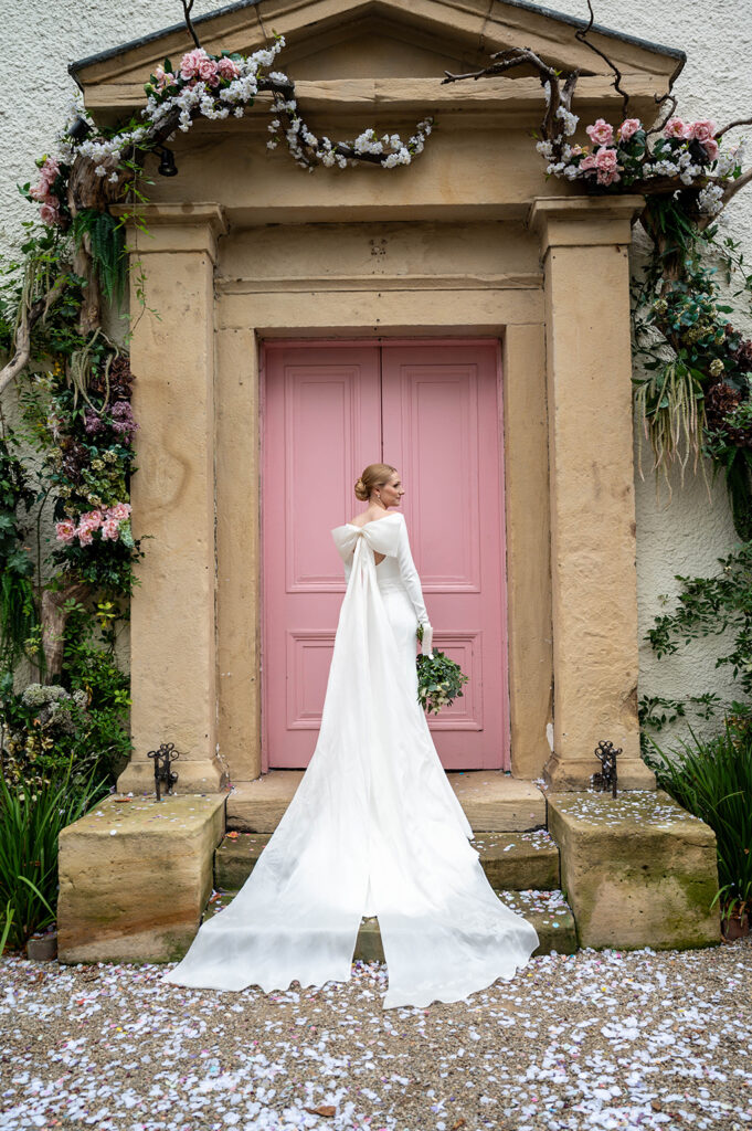 Bride in a stunning wedding dress standing in front of the pink door at The Croft Hotel in Darlington, photographed by Tees Valley Weddings.