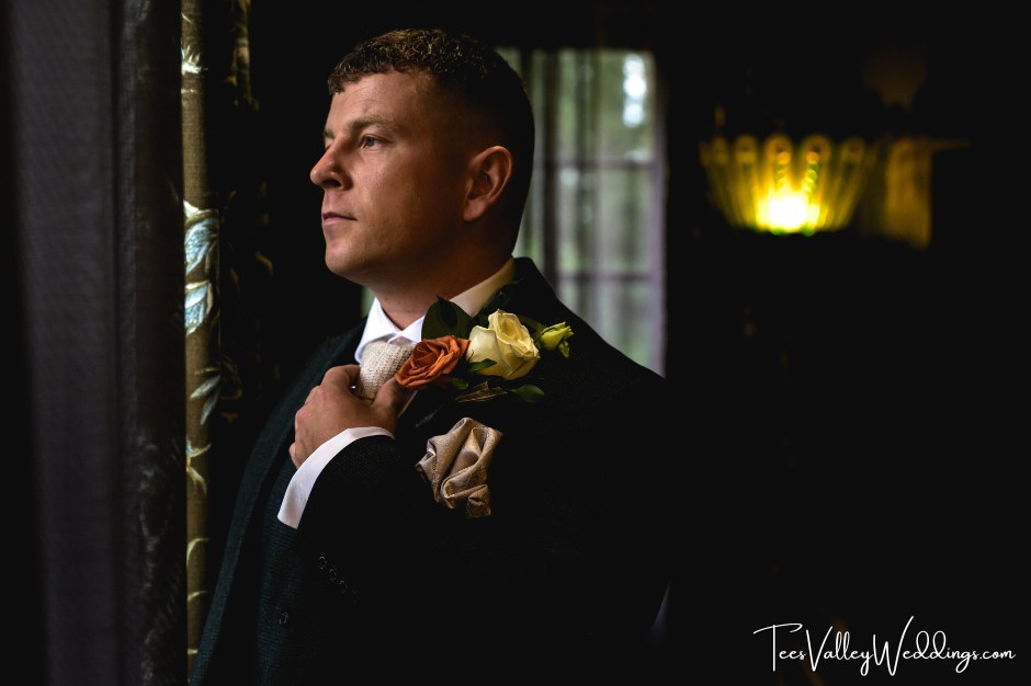 Groom smiling during buttonhole prep at Le Petit Château wedding venue.